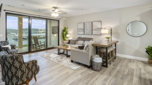 A modern living room with a sofa, armchairs, a coffee table, and a dining table. There is a large window with a view of a bridge and greenery. - Topsider Experience in the Heart of Osage Beach (Osage Beach)