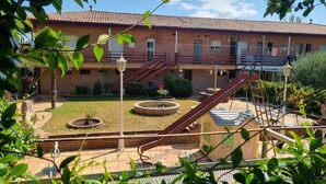 A brick building with a tiled roof, a staircase, and a small garden area with a fountain and seating.