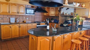 A kitchen with wooden cabinets, a black countertop, a microwave, and a large black range hood.