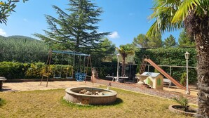 A playground with swings, a slide, and a small building with a red roof.