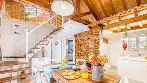 Une cuisine spacieuse avec une table en bois dressée pour le repas, un escalier menant à un niveau supérieur et un mur d’accent en pierre.