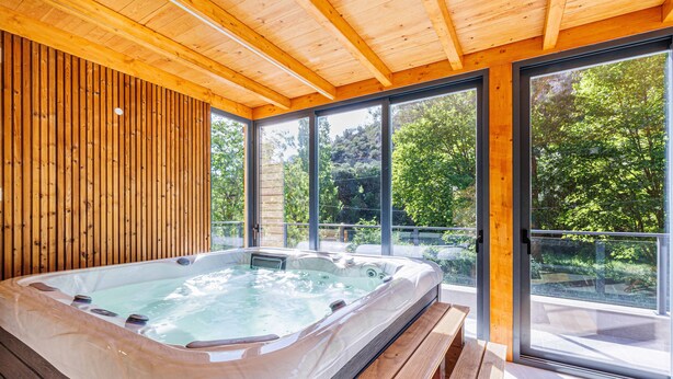 Un bain à remous dans un chalet en bois doté de grandes fenêtres et d’un banc.