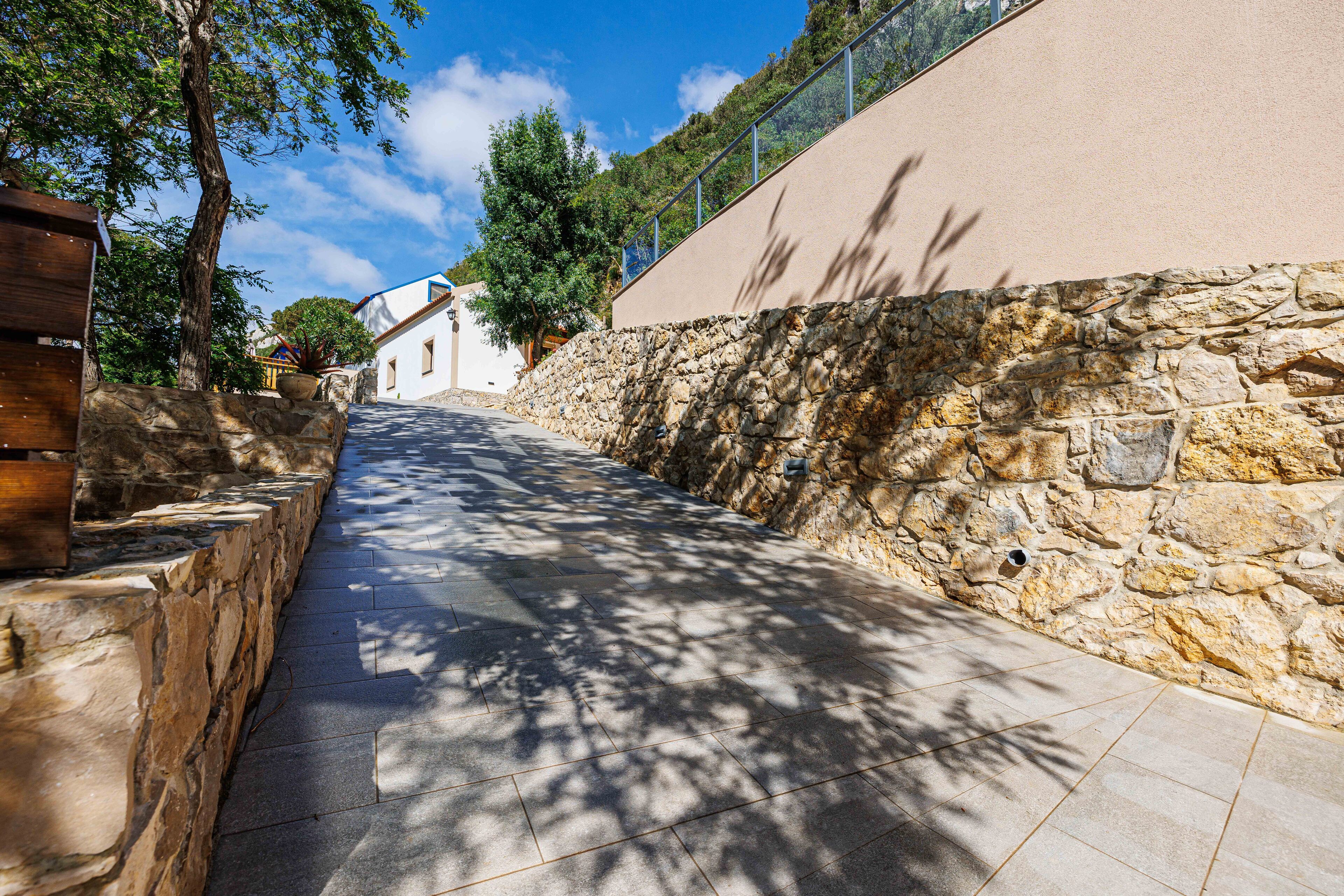 A stone pathway leading to a building with a stone wall on one side and a fence on the other.
