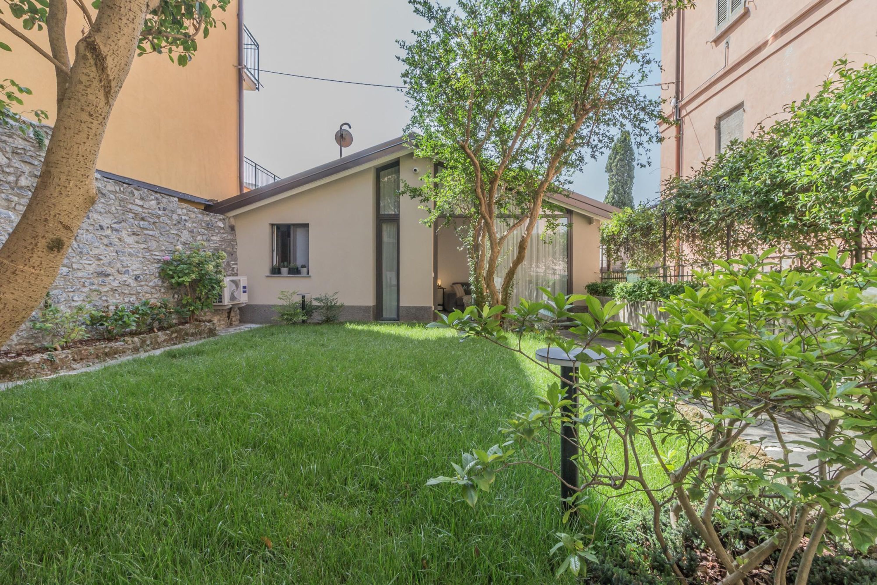 A small, single-story house with a sloped roof, a stone wall on one side, and a well-maintained lawn.