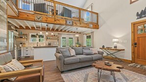 Ein geräumiger Wohnbereich mit hoher Decke, einer Holztreppe und einer Küche im Hintergrund.