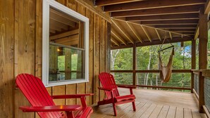Eine Holzhütte mit Veranda, zwei roten Adirondack-Stühlen und einer Hängematte.