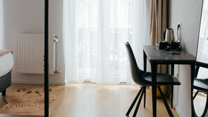 A modern hotel room with a bed, a desk with a chair, a flat-screen TV mounted on the wall, and a large window with sheer curtains. - Hôtel La Pièce  (Brussels)