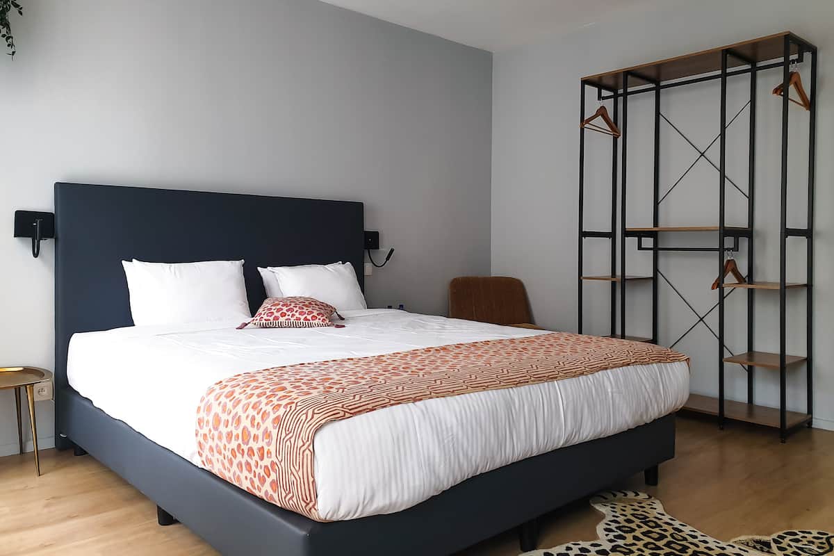 A modern bedroom with a dark headboard, a bed with patterned bedding, a small side table, and a wooden floor.