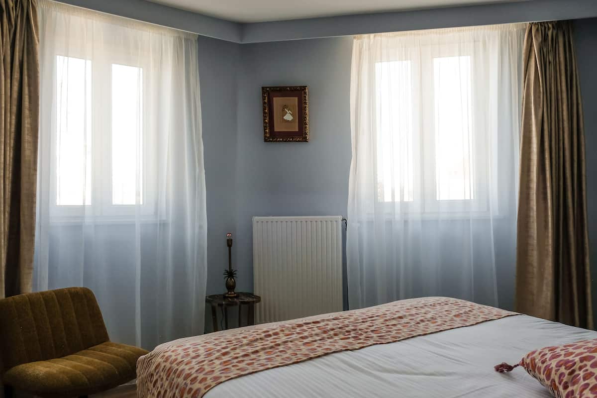 A bedroom with a bed, a chair, a radiator, and a picture on the wall.