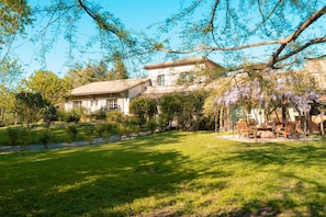 Ein Haus mit Garten, einer Terrasse mit Möbeln und einem Pergola mit violetten Blüten.