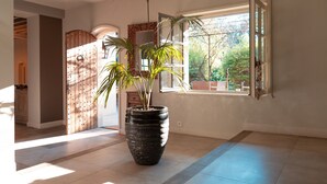 A room with a large potted plant, a window with a view of trees, and a wooden cabinet. - La Villa des Gones (Dommartin)