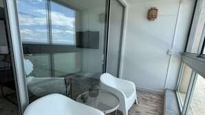 A balcony with two white chairs, a small round table, and a glass door leading to a dining area.