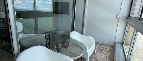 A balcony with two white chairs, a small round table, and a glass door leading to a dining area.