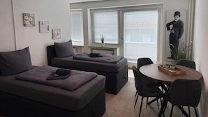 Una camera moderna con un divano letto, un tavolo da pranzo con sedie e un'ampia finestra con tende.