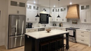 A modern kitchen with white cabinetry, stainless steel appliances, and pendant lighting.