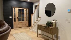 A hallway with a wooden door, a staircase, a round mirror, a wooden console table, and a brown leather couch.
