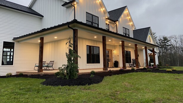 A two-story house with a covered porch, a landscaped front yard, and a large window on the second floor.