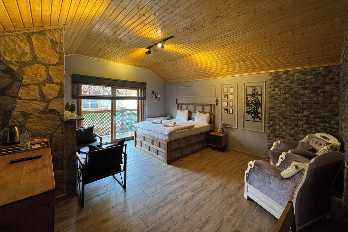 A cozy bedroom with a stone wall, a wooden ceiling, a bed, a desk, and a chair.