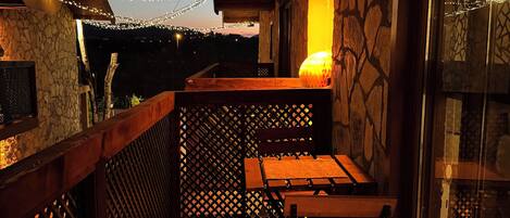 A wooden balcony with stone walls, string lights, and a table with chairs.
