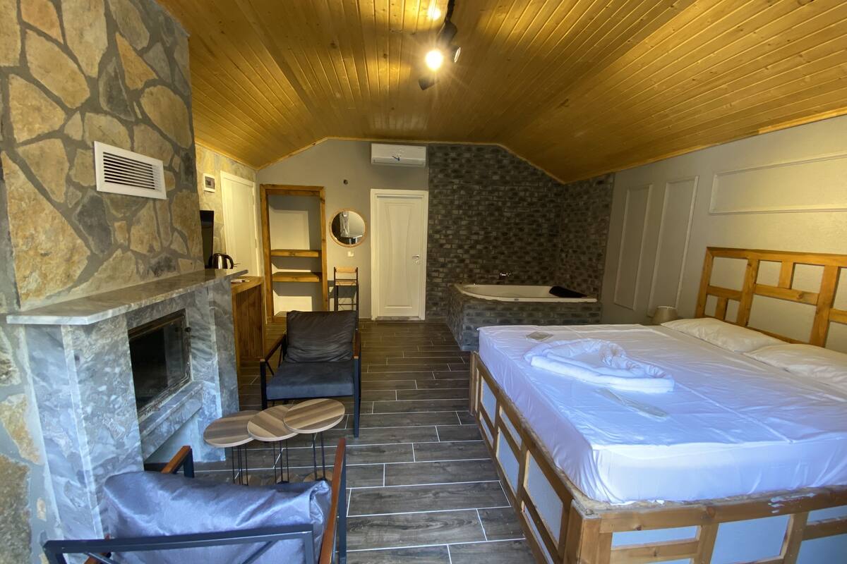 A bedroom with a stone fireplace, a wooden bed, a small seating area, and a stone wall.