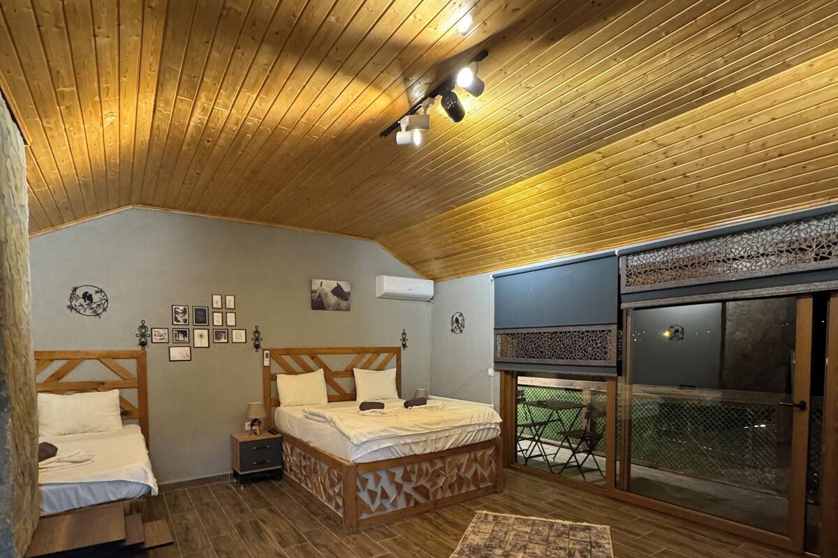 A bedroom with two beds, a wooden ceiling, and a view of the outside.