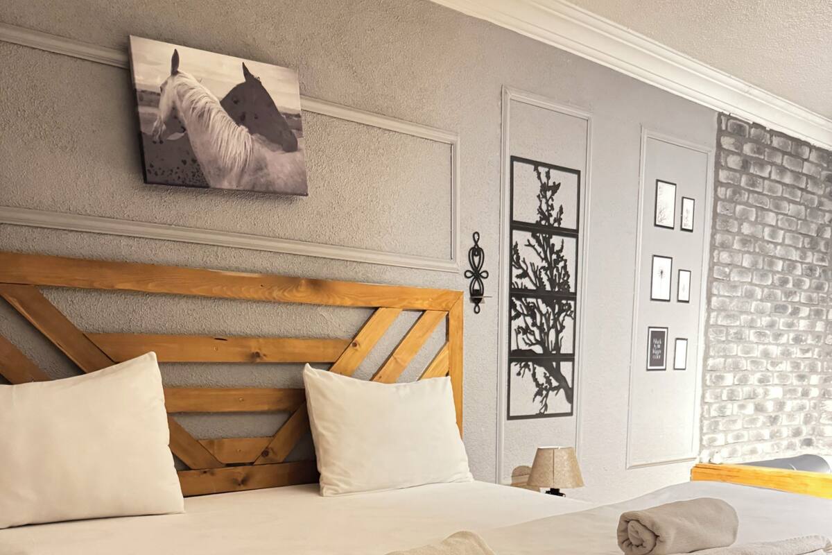 A neatly made bed with white linens and two rolled towels, a wooden headboard, and a wall-mounted picture of horses.