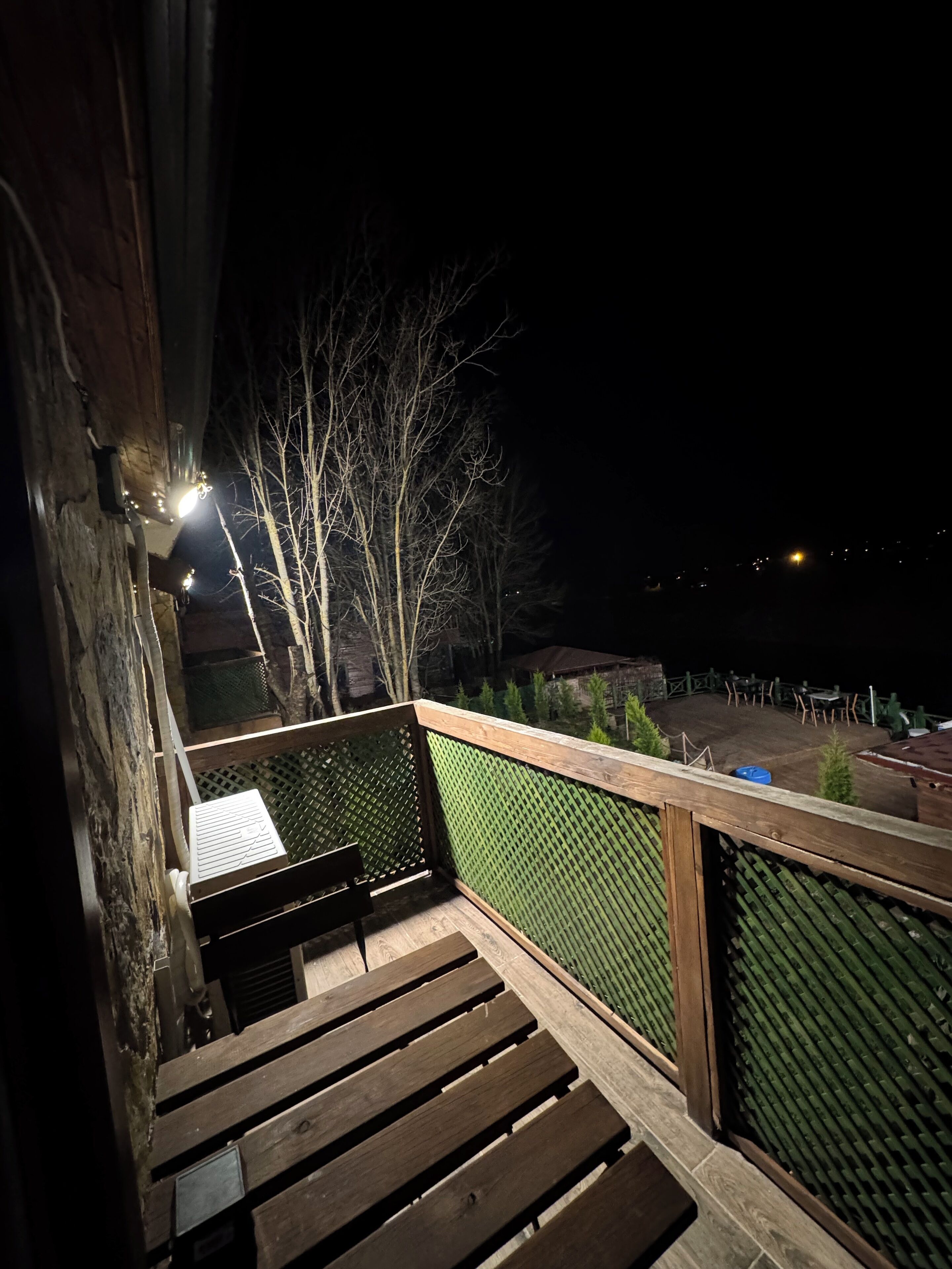 Una escalera de madera que conduce a un balcón con barandilla de malla verde.