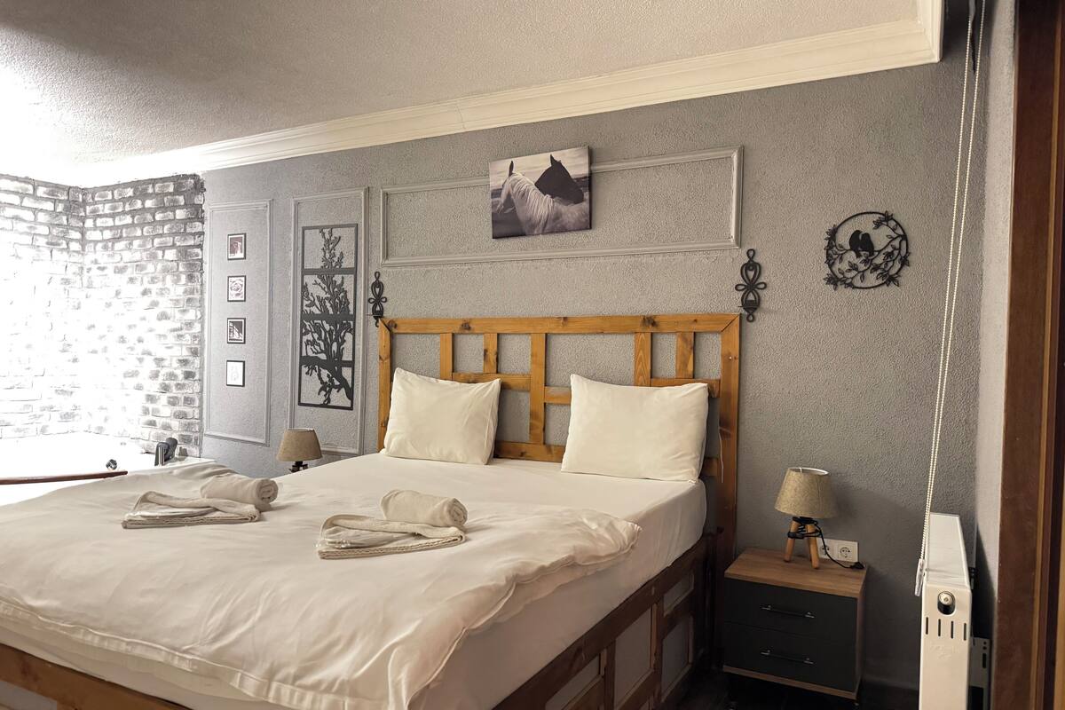 A neatly made bed with pillows and a blanket, a bedside table with a lamp, a wall with framed pictures, and a decorative wall piece.