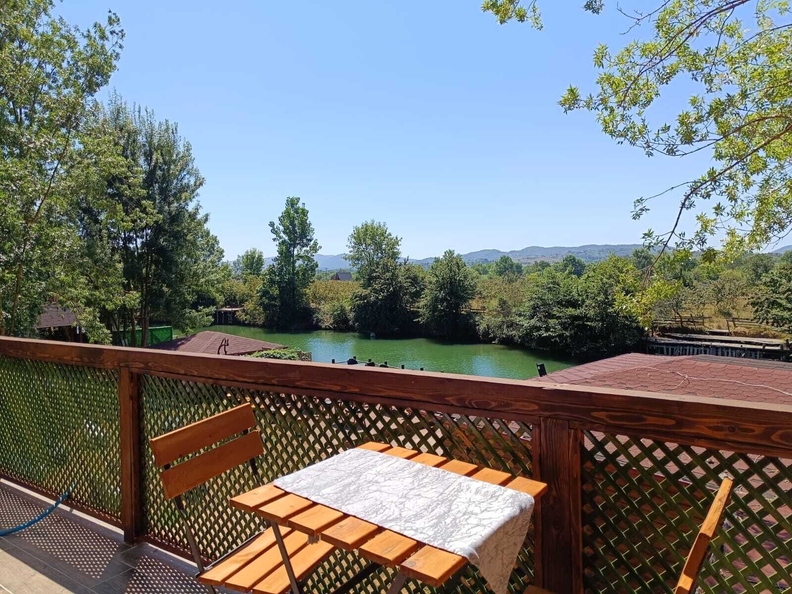 A wooden deck with a table and chair overlooking a river and forested hills.