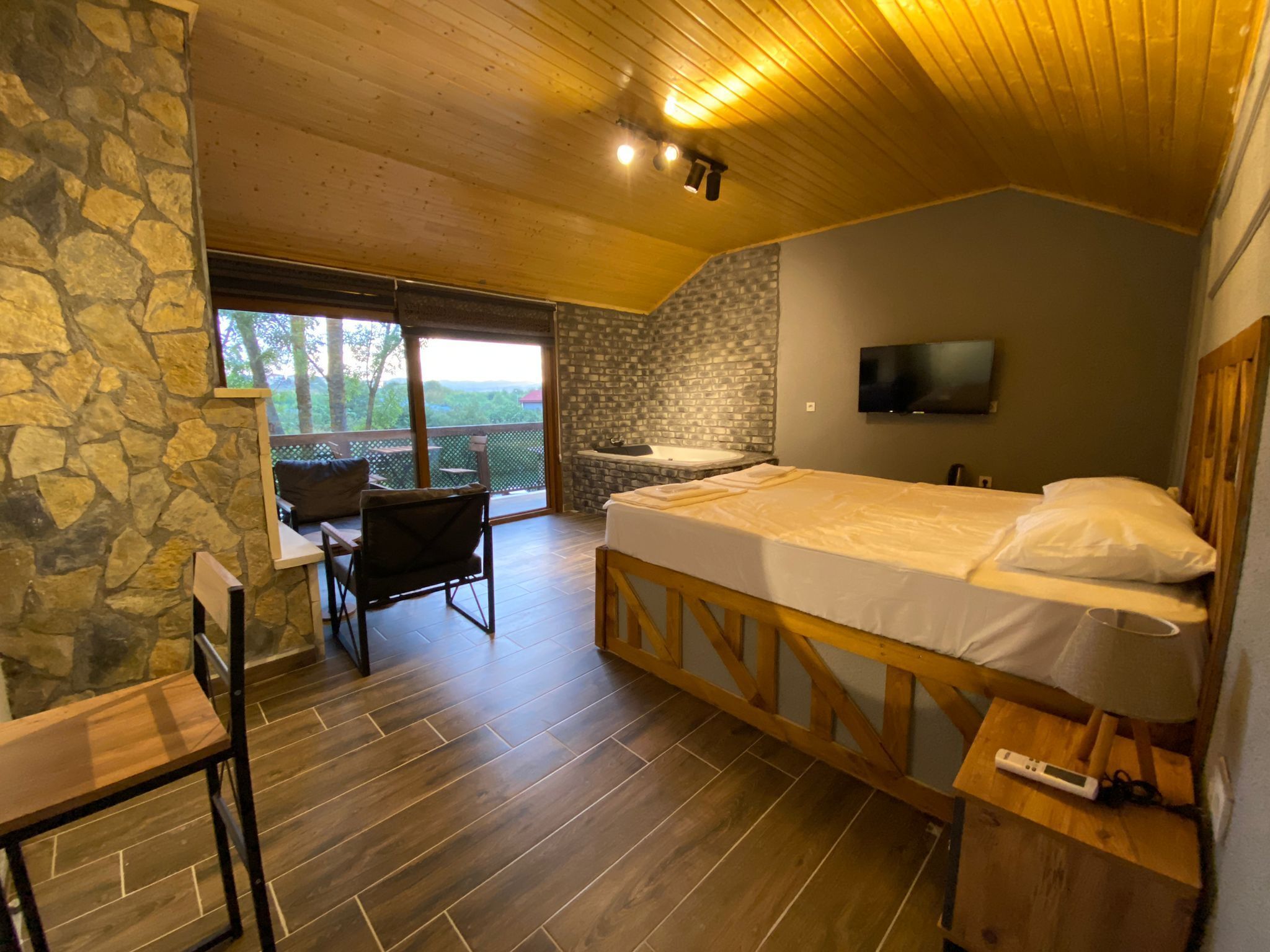 Un dormitorio con cama, escritorio, silla, televisor y pared de piedra.