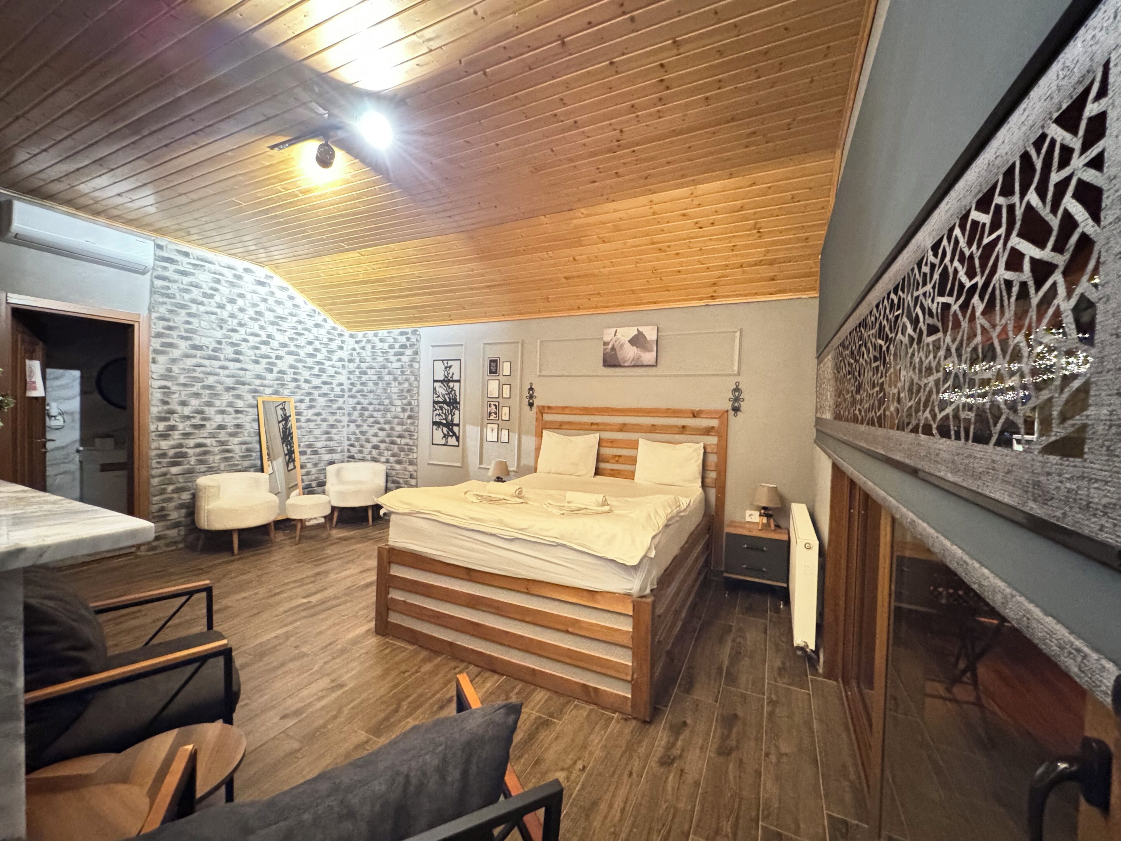 Un dormitorio con techo de madera, una cama con ropa blanca, una pared de piedra y un separador decorativo.
