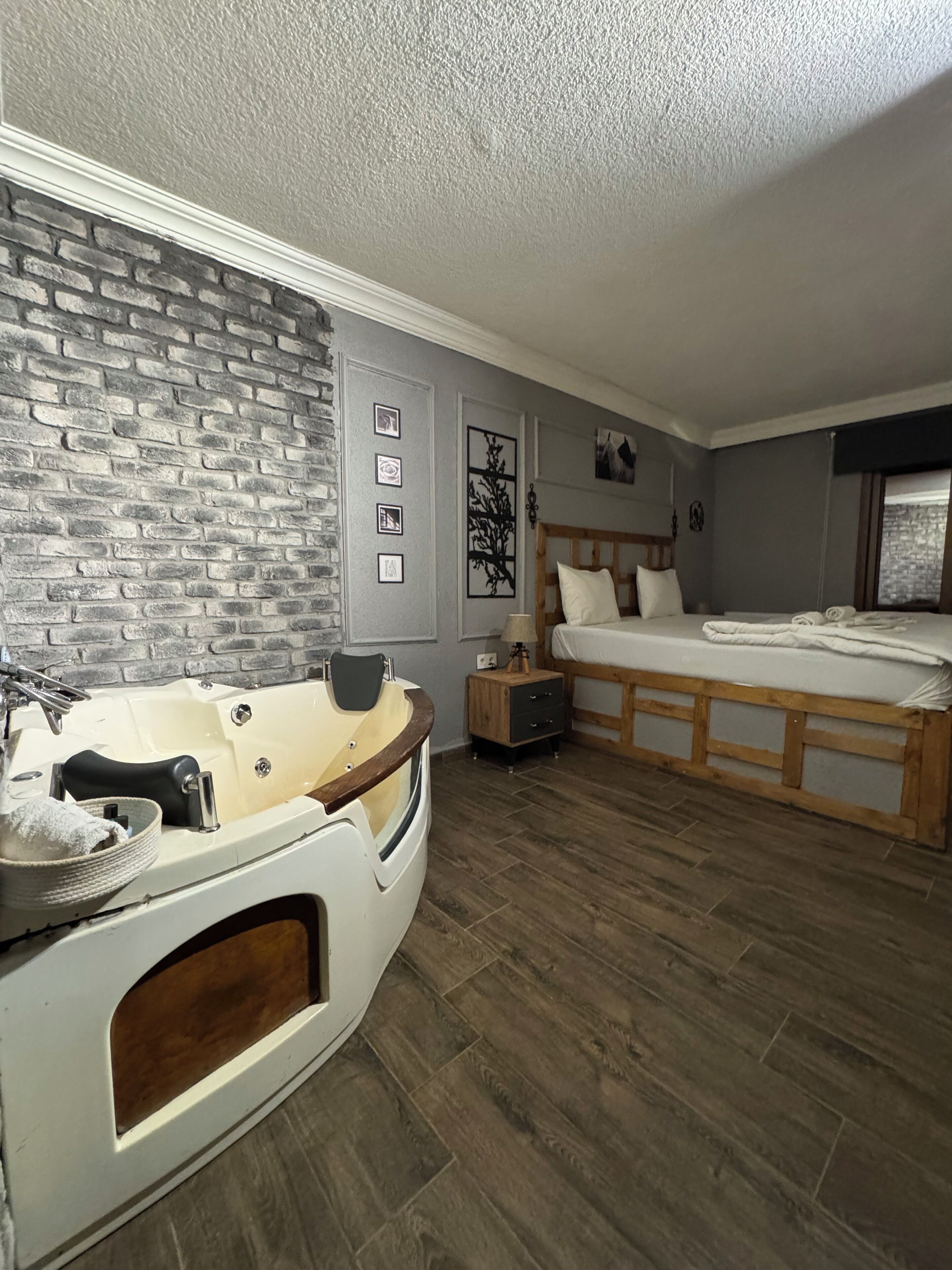 A modern bedroom with a wooden floor, a large bed, a smaller bed, a bathtub, and a brick wall.