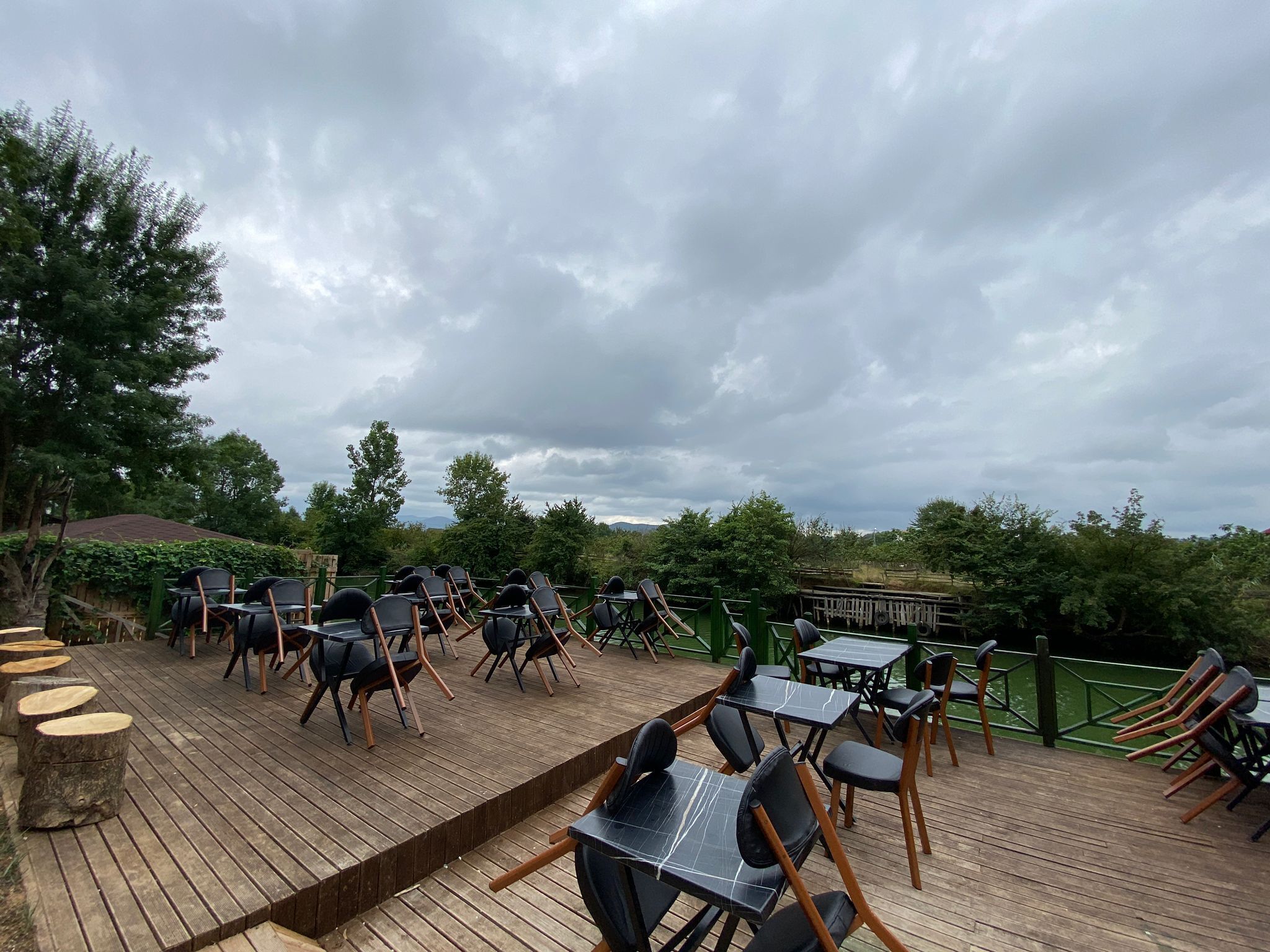 Un área de estar al aire libre con mesas y sillas, rodeada de follaje y una terraza de madera.