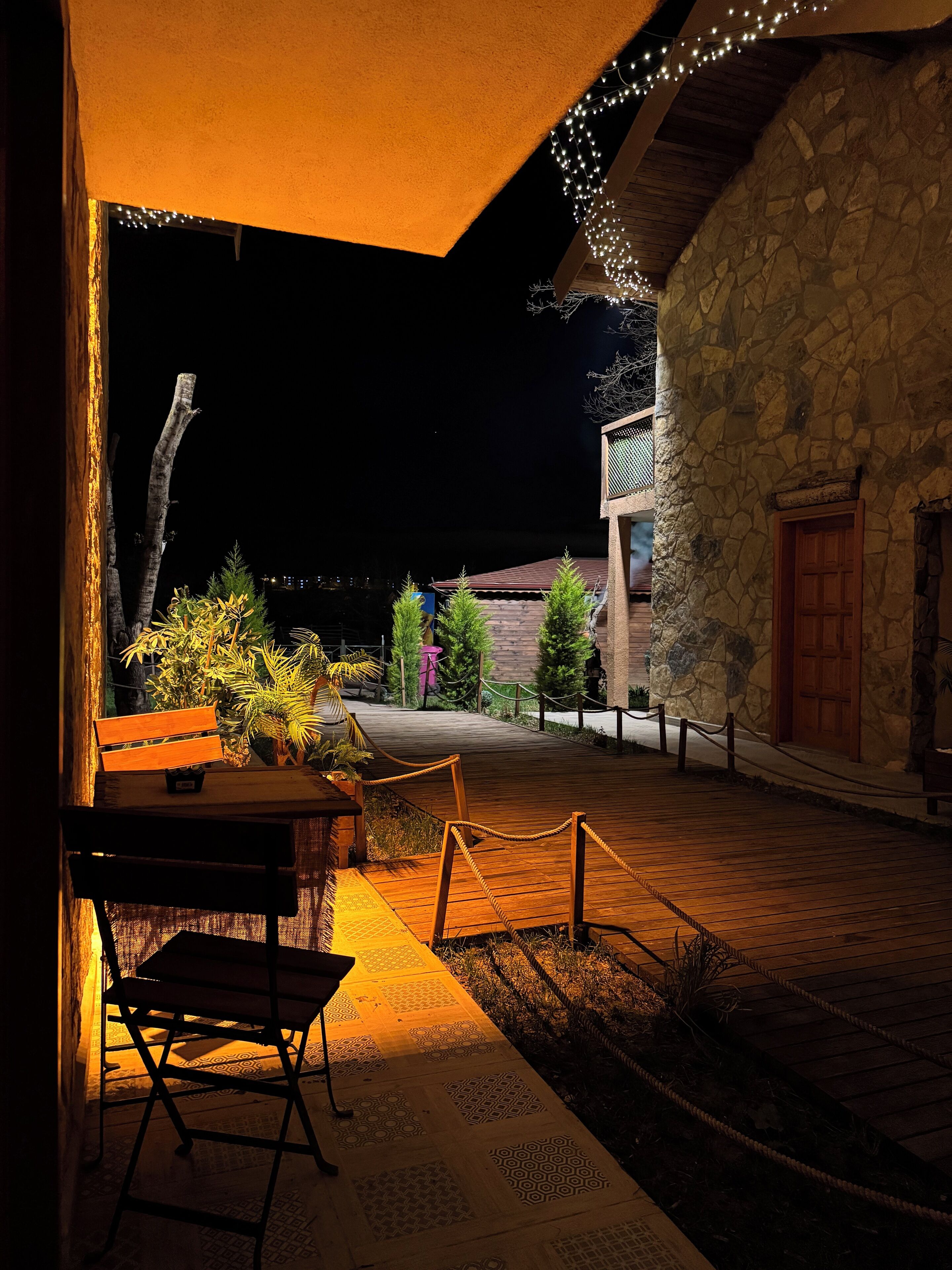 A courtyard with a wooden bench, potted plants, and a stone wall.