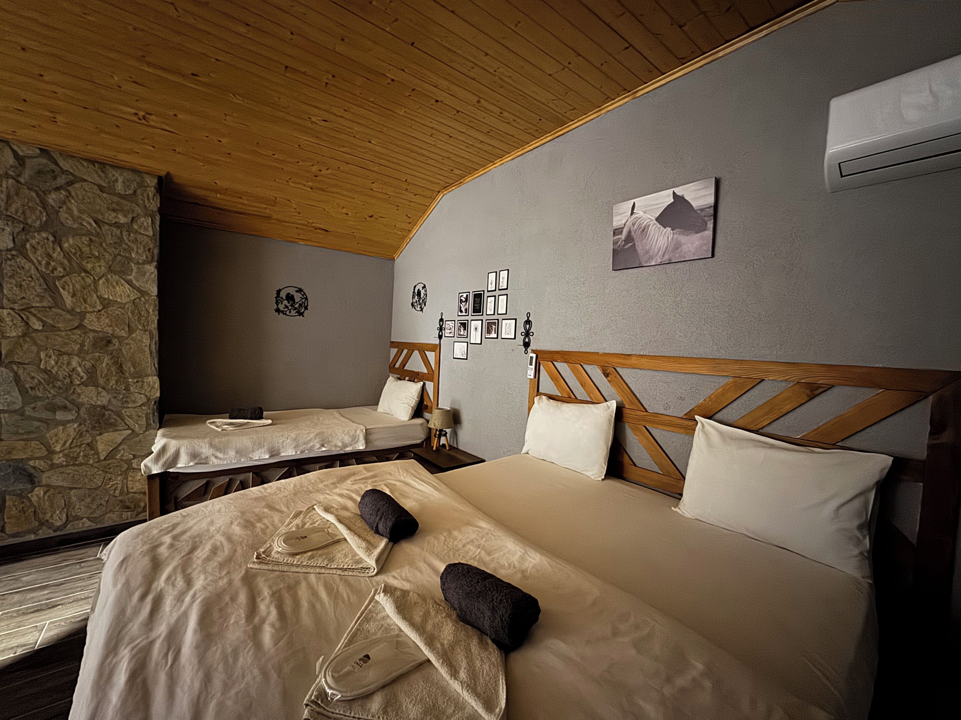 A room with two beds, a stone wall, wooden ceiling, and a picture on the wall.