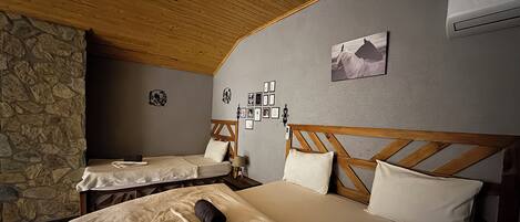 A room with two beds, a stone wall, wooden ceiling, and a picture on the wall.