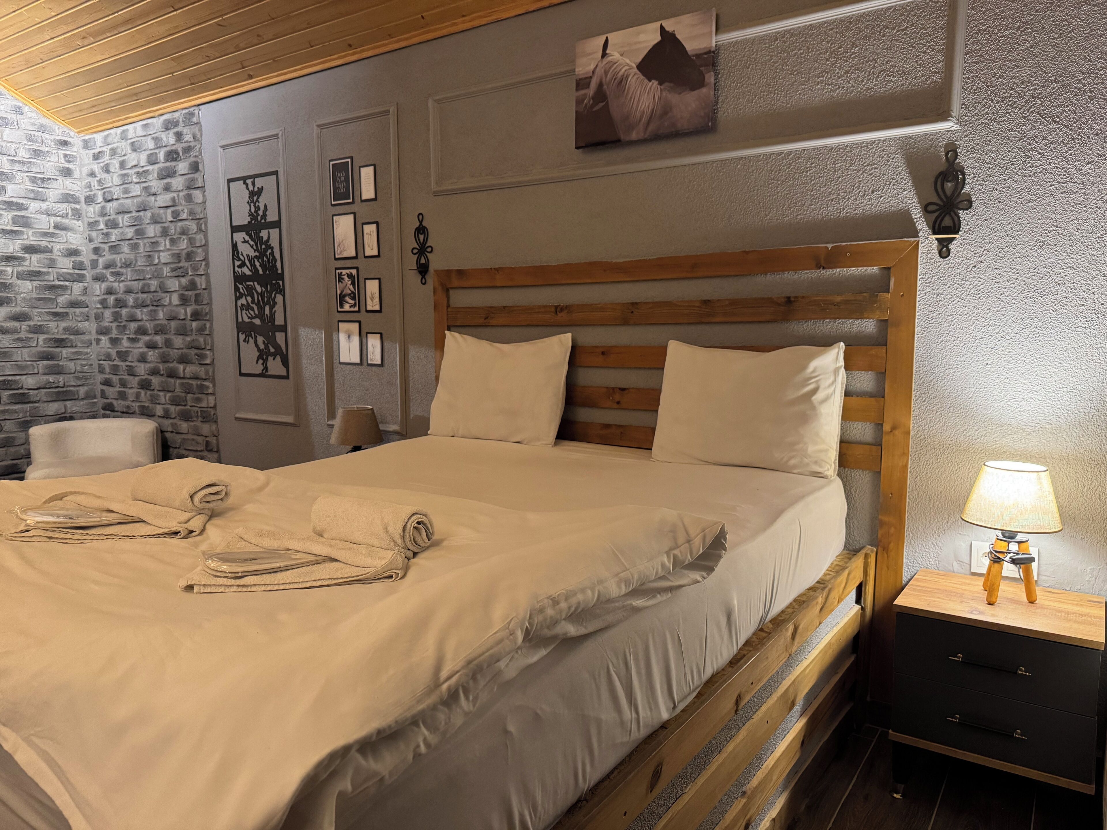 A neatly made bed with a wooden headboard, a small bedside table with a lamp, and a wall with framed pictures.