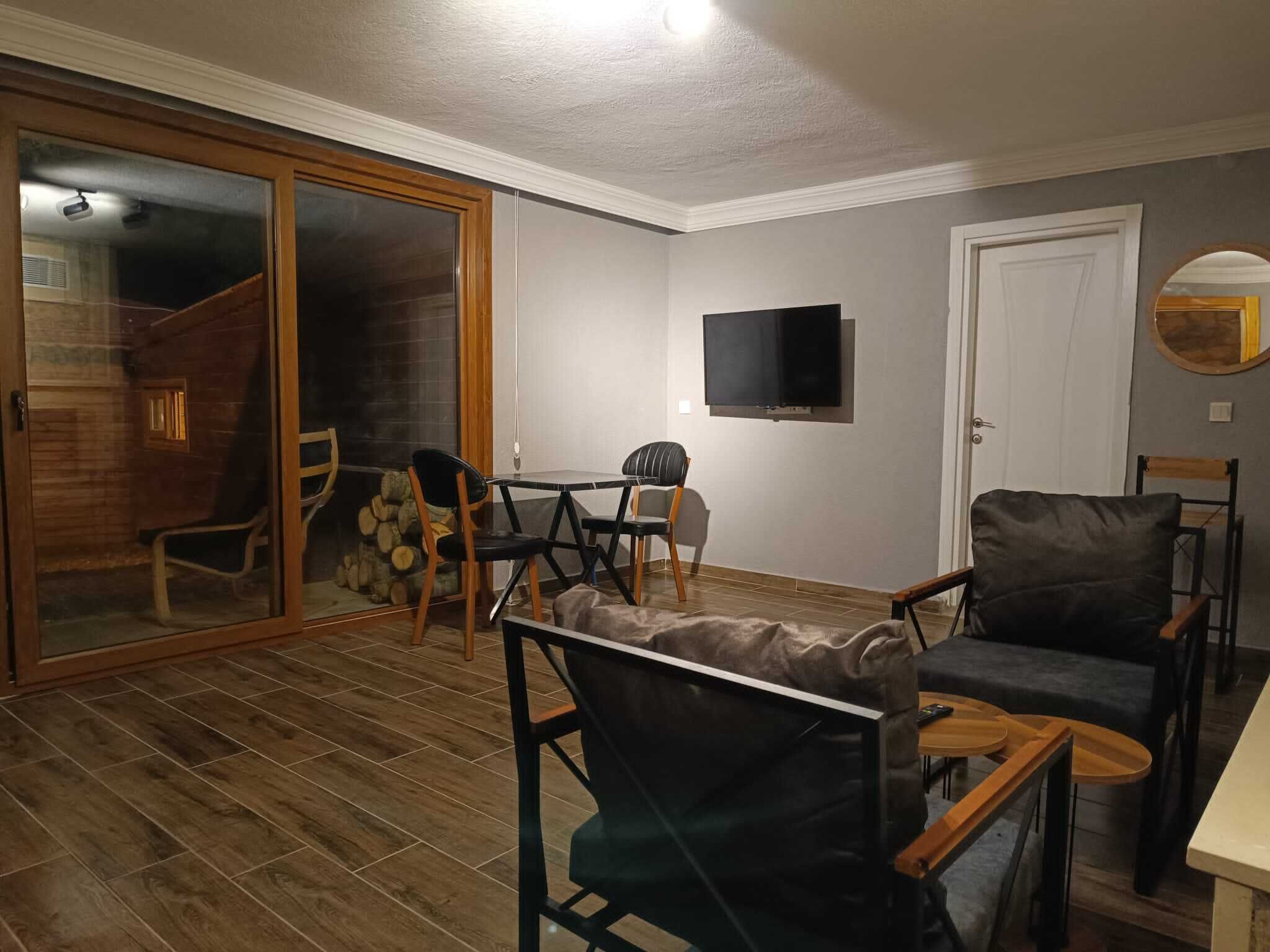 A living room with a sliding glass door leading to a balcony, a flat-screen TV mounted on the wall, and a dining area with a table and chairs.