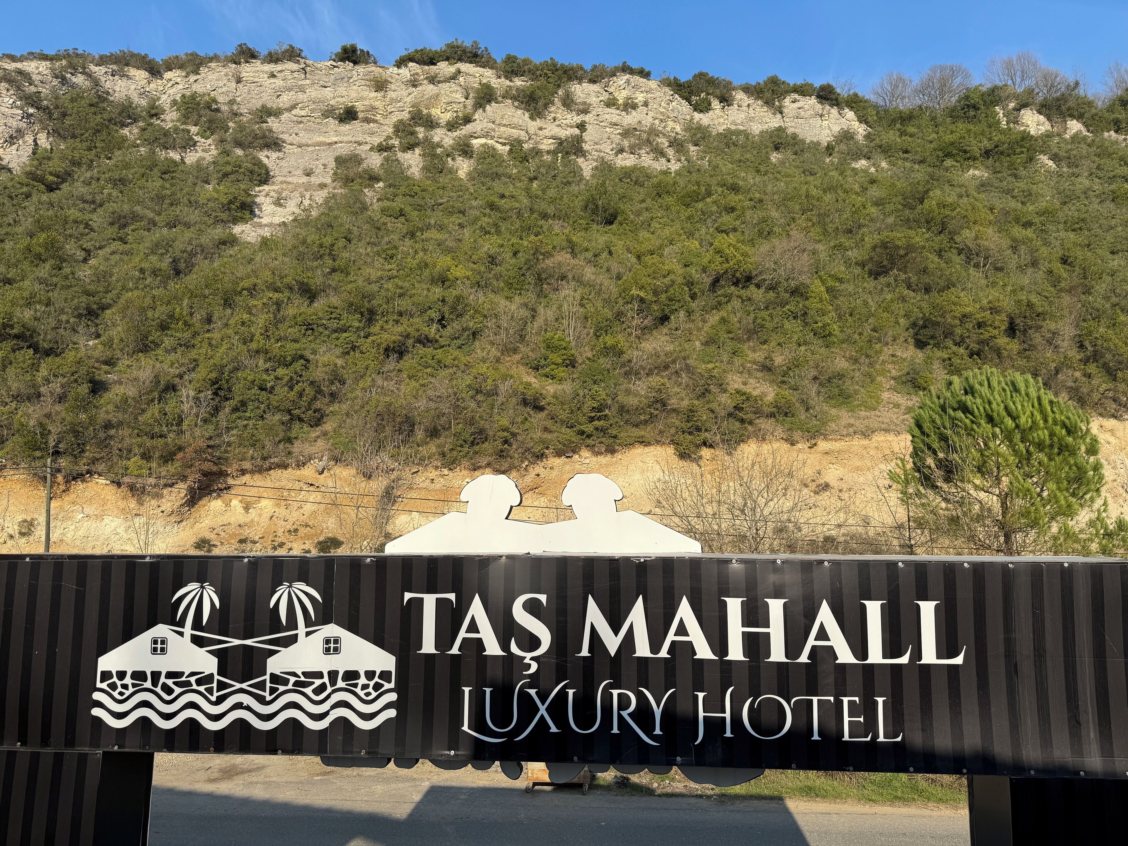 A sign for the Tas Mahall Luxury Hotel with a coastal scene in the background.