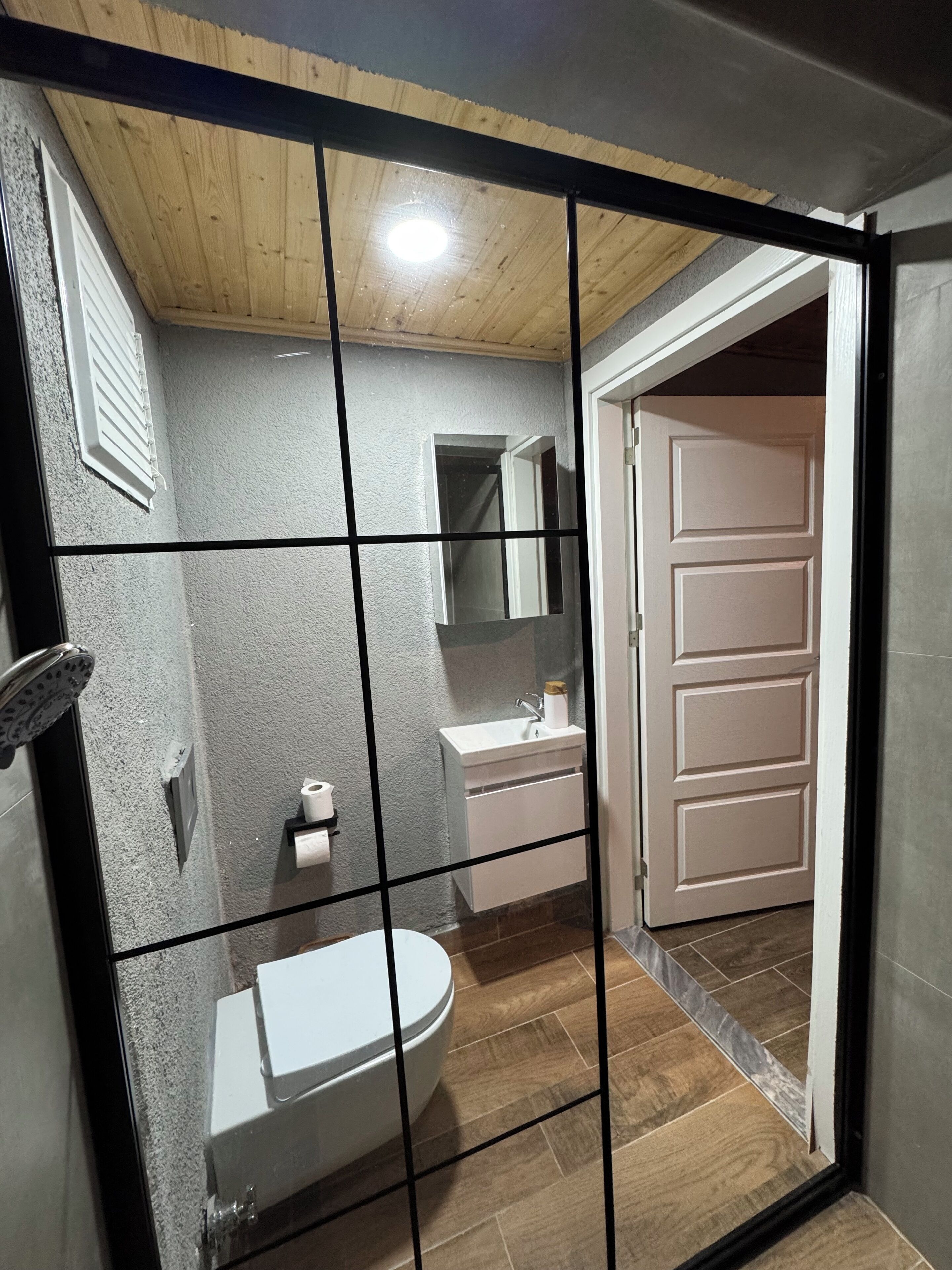 A bathroom with a wooden ceiling, a white sink, a mirror, and a toilet.