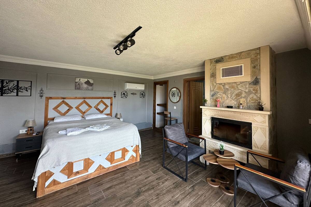 A bedroom with a bed, a fireplace, a chair, a nightstand, and a wall-mounted air conditioner.