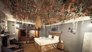 A bedroom with a wooden bed, a nightstand, a chair, a fireplace, and a bathroom with a sink. - Taş Mahall Luxury Hotel (Sile)