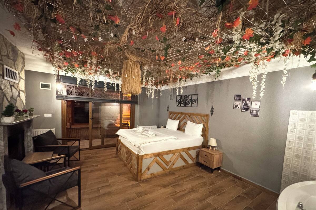 A bedroom with a wooden bed, a nightstand, a chair, a fireplace, and a bathroom with a sink.