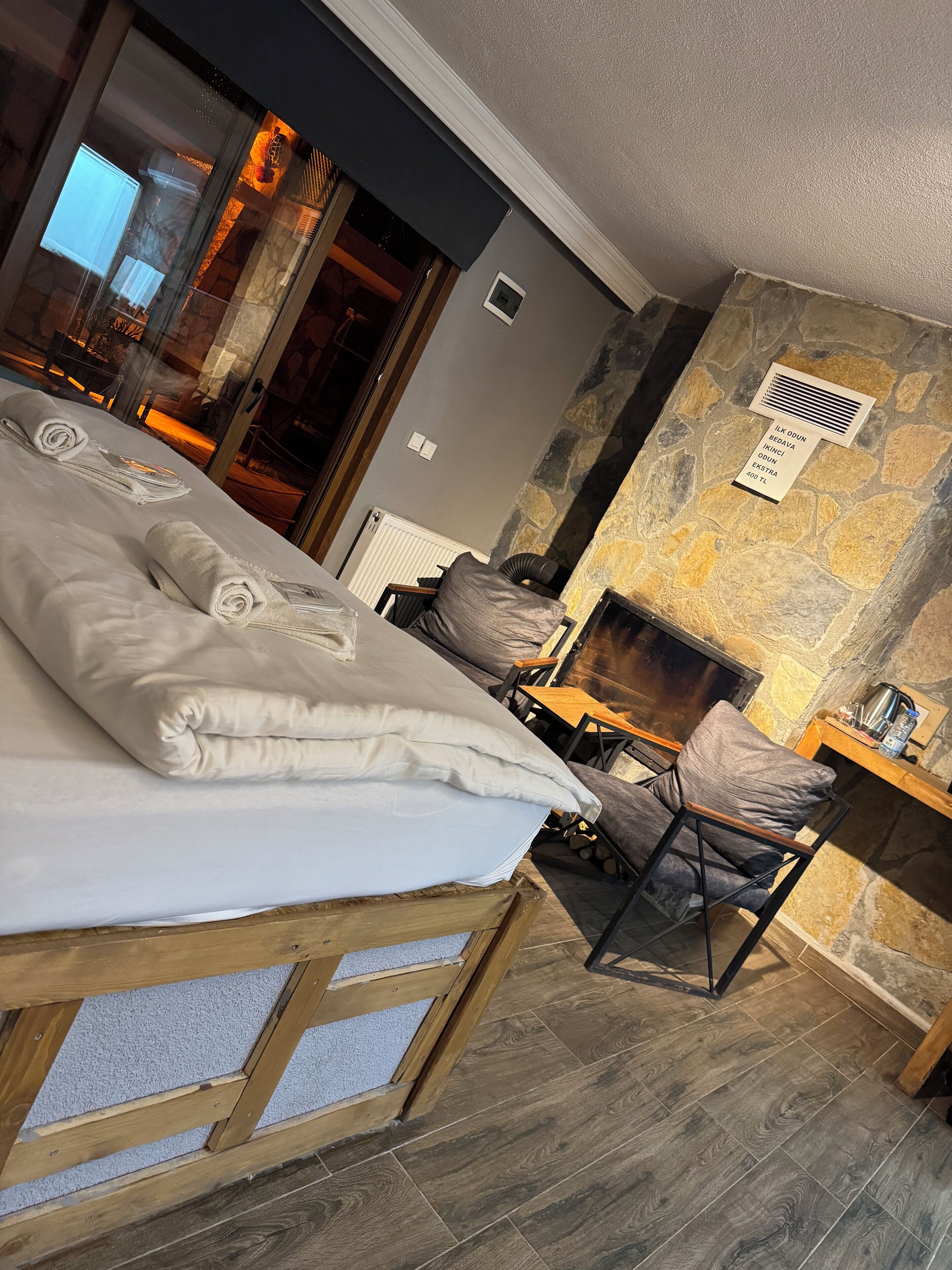Ett hotellrum med en säng, en trästol, en vägg av sten och en öppen spis.