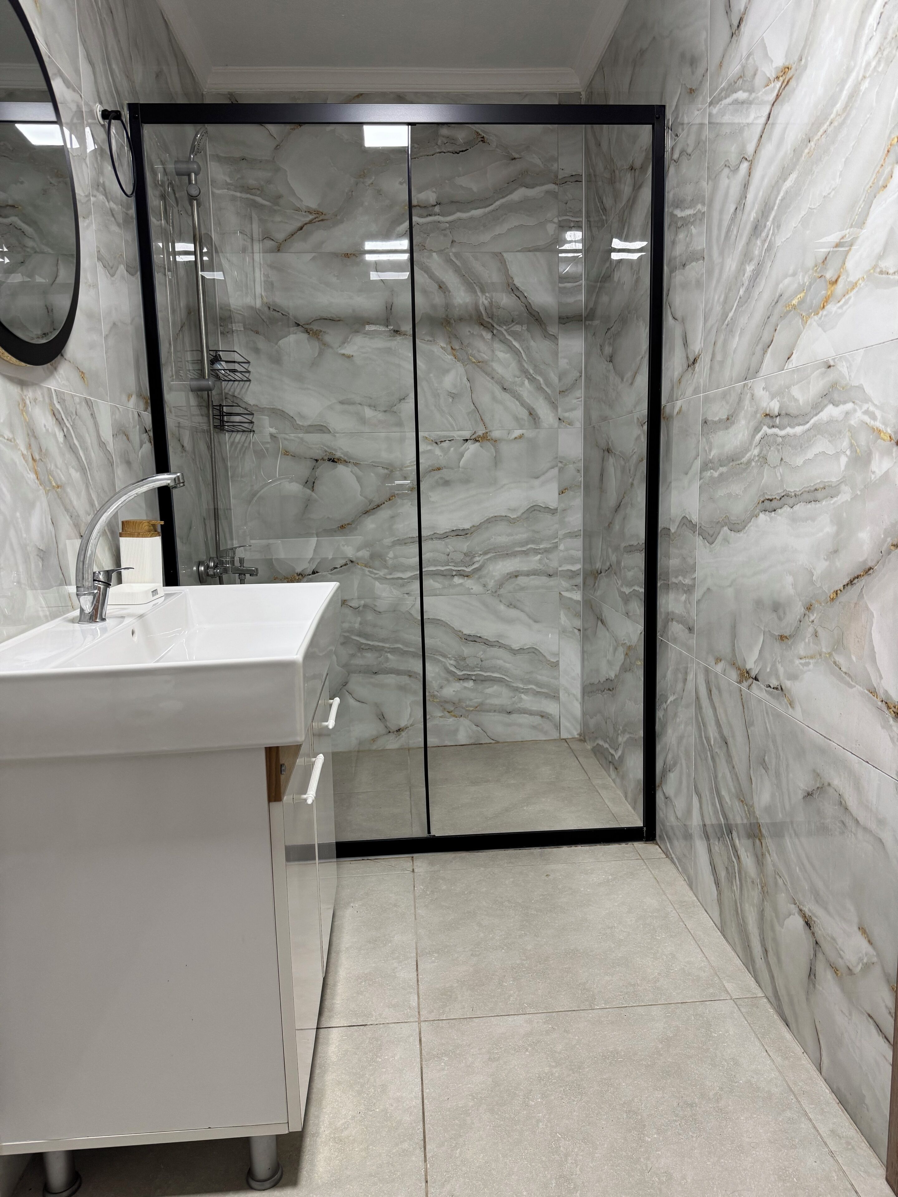 A bathroom with a glass-enclosed shower, a white sink, and marble walls.
