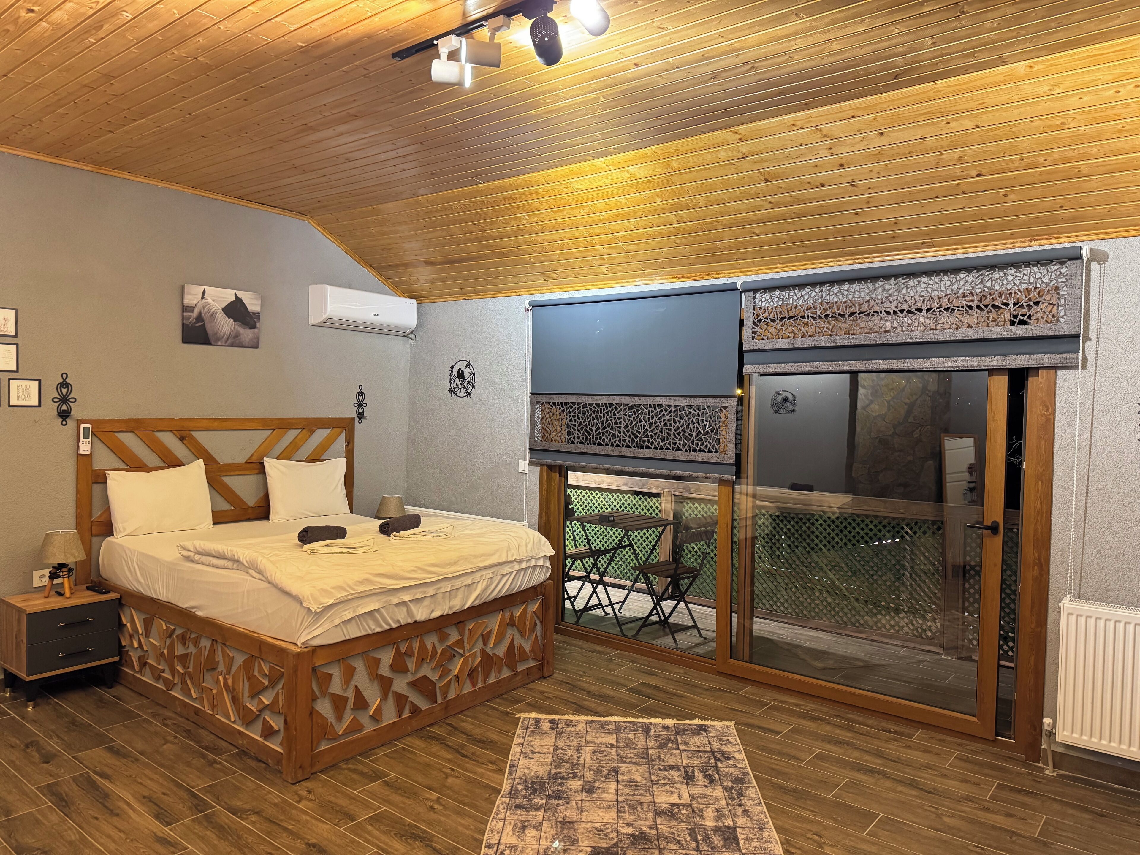 Un dormitorio con techo de madera, una cama con cabecera, aire acondicionado, una lámpara de pared y una puerta corrediza de vidrio que da a un área exterior.