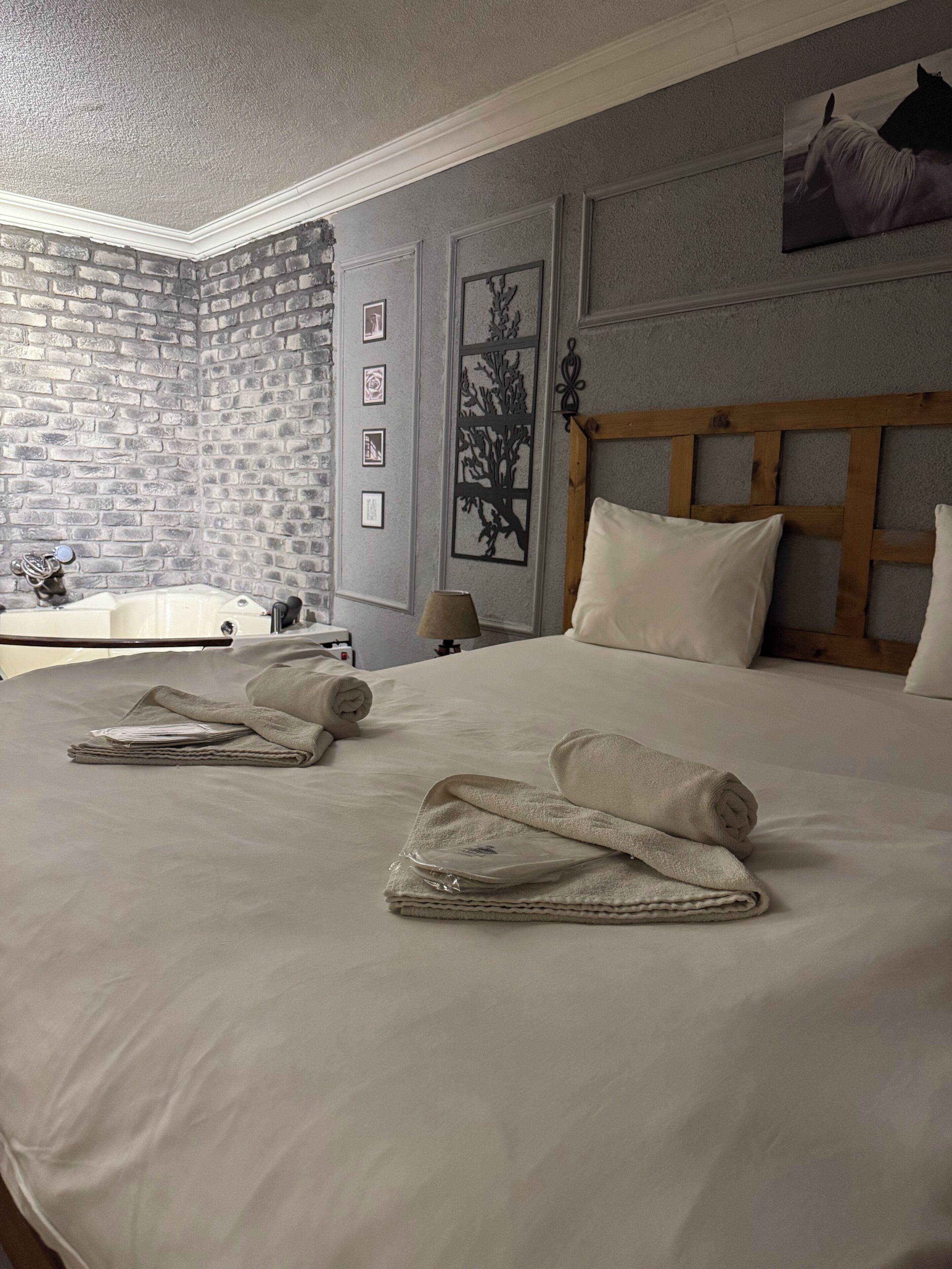 A neatly made bed with towels, a wooden headboard, and a wall with framed pictures and a tree cutout.