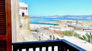 A coastal view from a balcony with a clear sky, a road, and a distant shoreline with buildings and a pier.