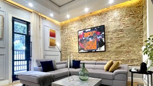 A modern living room with a sectional sofa, a coffee table, and a large abstract painting on the brick wall.