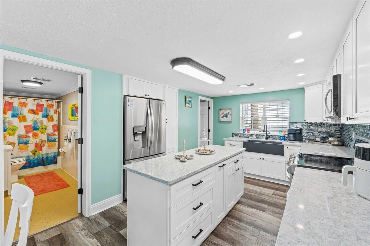 A modern kitchen with white cabinetry, a stainless steel refrigerator, and a granite countertop.